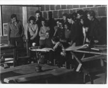 Josef Albers' drawing class, Black Mountain College. From the back of the photograph: "Albers, seated; Eva Zhitlowsky, seated at Albers's left; Faith Murray, standing behind Albers, against wall, with bangs and glasses; Claude Stoller, third from right, against wall." Photograph likely taken at the Blue Ridge campus. Courtesy of Western Regional Archives.