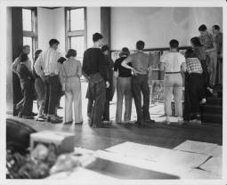 Josef Albers's Drawing Class, Black Mountain College, ca. 1939-1940. From the back of the photograph: "left to right (incomplete listing): Charles Kessler (extreme left, hand on hip), Hope Stephens (in straight skirt and the saddle shoes), Betty Brett (leaning forward, standing in fron of male student with pencil behind his ear), Frances Kuntz (beside Brett), Dick Andrews (with pipe), Fred Stone (in front of Andrews), Mimi French (in dark sweater and light collar), Robert De Niro (hand on hip, moccasins), Bela Martin (t-shirt and sneakers), Martha McMillan (light plaid shirt and sneakers with dark socks), Harriet Englehardt (dark plaid shirt, light socks, standing on second and third steps), Rudolph Haase (sitting on banister)." Photograph likely taken at the Blue Ridge campus. Courtesy of Western Regional Archives.